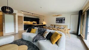 Un salon moderne avec un canapé gris, une table basse en bois et un coin repas comprenant une table et des chaises en bois.