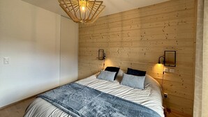 Une chambre avec un mur en bois, un lit recouvert d’une couverture grise, deux lampes de chevet et un luminaire au plafond au design original.