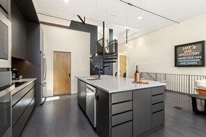 Une cuisine moderne dotée d’un îlot central, d’appareils électroménagers en acier inoxydable et d’une enseigne publicitaire pour des services de retapisserie.