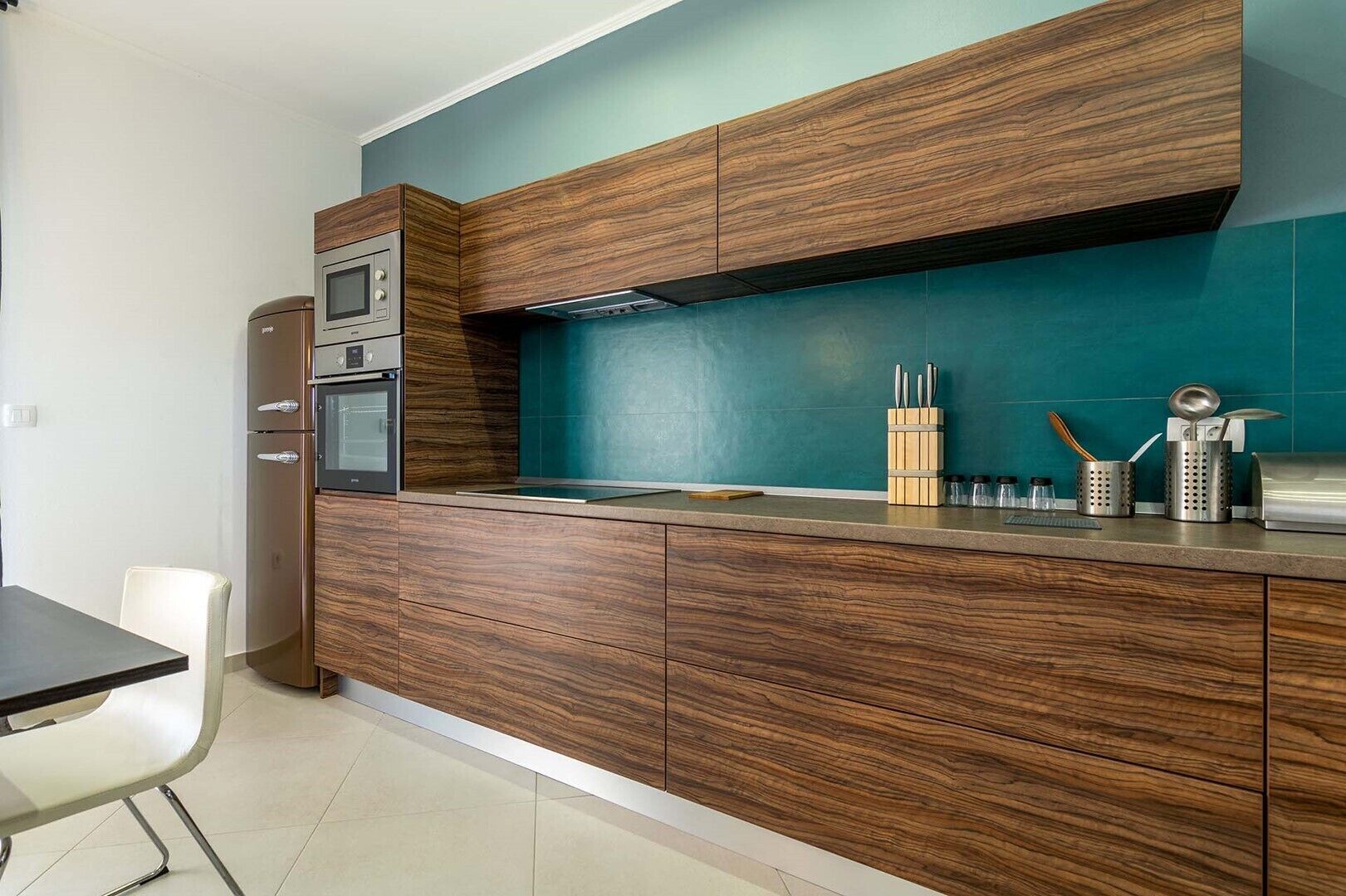 Une cuisine moderne avec des armoires en bois, un four encastré et un pare-feu de couleur turquoise.