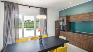 A modern kitchen with a dining area, featuring a large table, yellow chairs, and a view of a swimming pool. - Villa Jan in Valbandon (Valbandon)