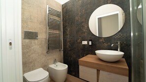 A modern bathroom with a white toilet, a bidet, a sink with a large mirror, and a towel rack. - Manere Suites (Palermo)