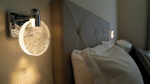 A modern bedroom with a headboard, a wall-mounted light fixture, and a bed with white bedding. - Manere Suites (Palermo)