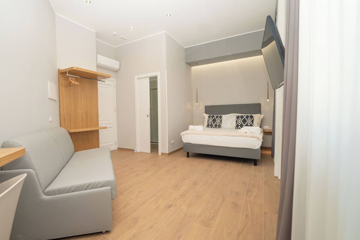 Una camera da letto moderna con un divano grigio, un letto con cuscini decorati e un armadio in legno.