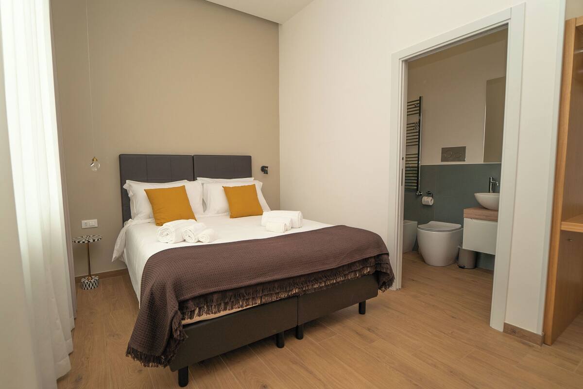 Una camera da letto ordinata con un letto, un comodino e vista sul bagno.