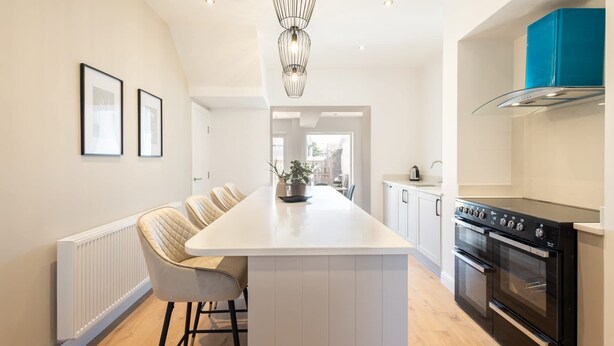 A modern kitchen with a central island, white cabinetry, a black stove, and a blue accent wall. - Host & Stay | Hithe House (Amble)