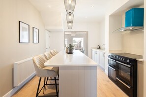 A modern kitchen with a central island, white cabinetry, a black stove, and a blue accent wall. - Host & Stay | Hithe House (Amble)