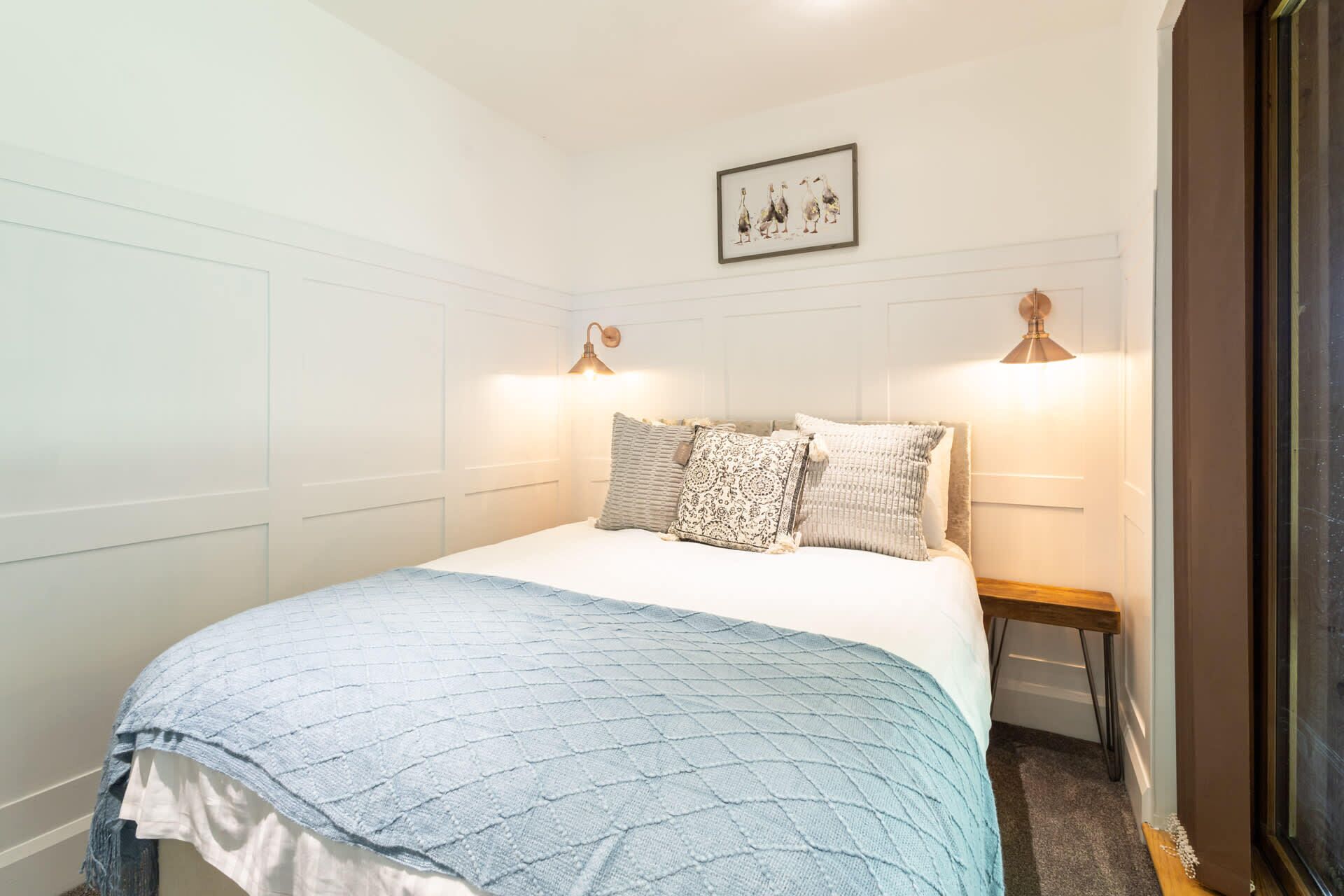 A neatly arranged bedroom with a bed, pillows, and two wall-mounted lamps.