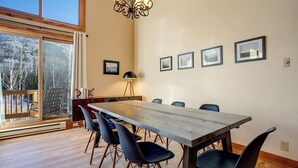 Un coin repas avec une grande table en bois, six chaises et un lustre.