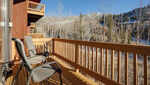 Une terrasse en bois avec deux chaises et une table, offrant une vue sur un paysage montagneux parsemé d’arbres.