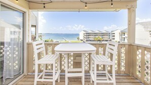 Un balcon avec une table et des chaises blanches, donnant sur une plage et l’océan.