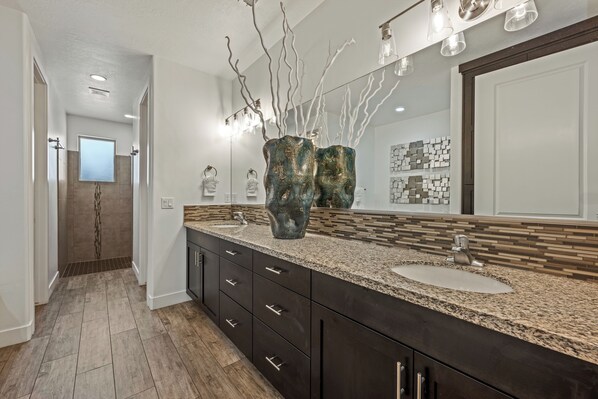 A modern bathroom with a large mirror, granite countertop, and a decorative vase.