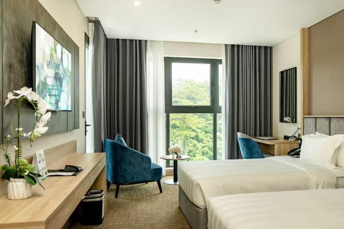 A modern hotel room with a large bed, a desk, a chair, and a view of greenery through the window.