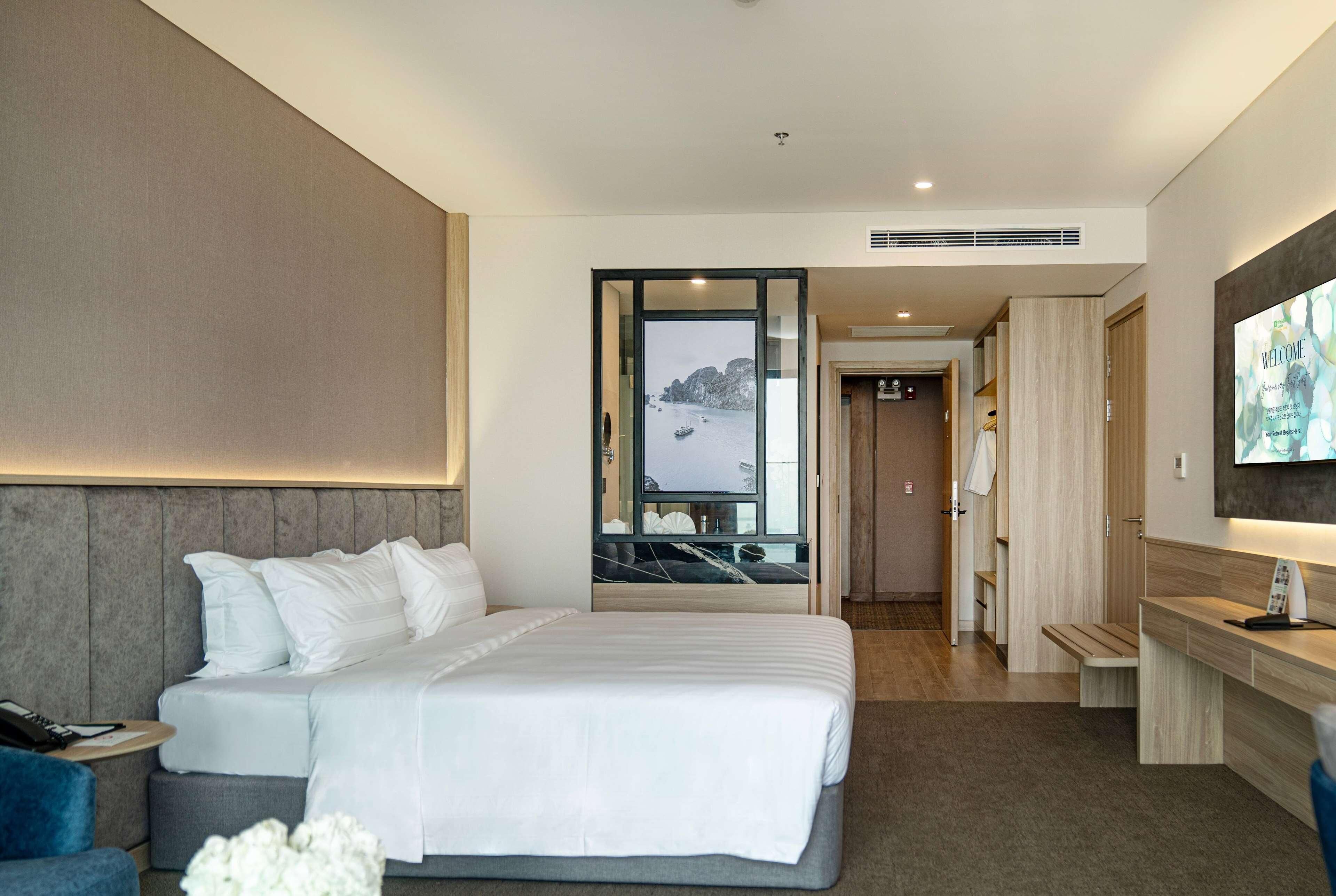 A hotel room with a bed, a desk, a TV, and a view of the sea.