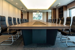 A conference room with a long table, black chairs, a projector screen, and a welcoming message. - Wyndham Garden Legend Halong (Bai Chay)