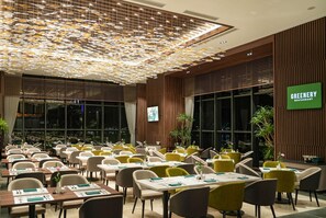 A restaurant with a modern interior, featuring a unique ceiling design, multiple dining tables with chairs, and a sign indicating the restaurant name. - Wyndham Garden Legend Halong (Bai Chay)