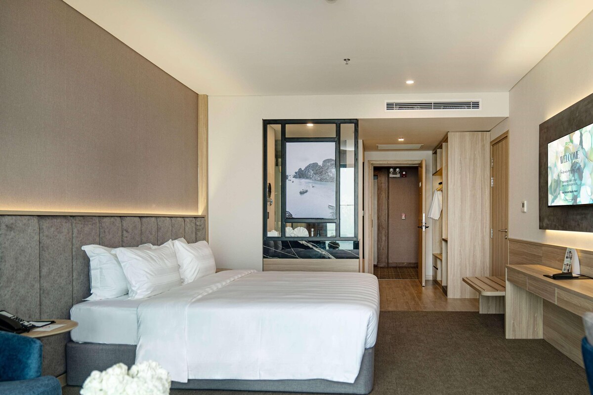 Une chambre d’hôtel avec un lit, un bureau, une télévision et une vue sur la mer.