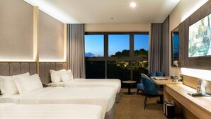A hotel room with two beds, a desk, a chair, a TV, and a large window with a view. - Wyndham Garden Legend Halong (Bai Chay)