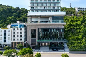 A modern hotel with a glass facade, a rooftop terrace, and a landscaped garden entrance. - Wyndham Garden Legend Halong (Bai Chay)