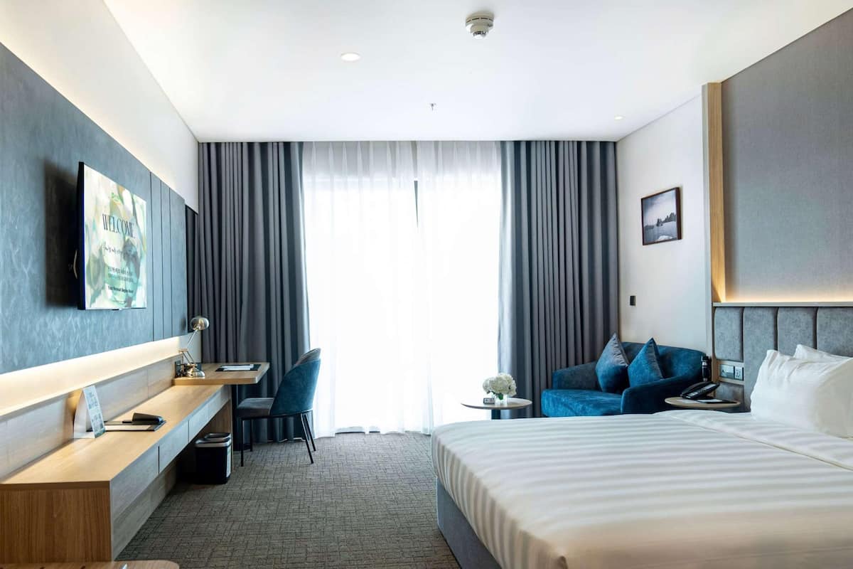 A hotel room with a bed, a desk, a chair, a small table, and a TV mounted on the wall.