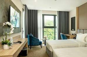 A modern hotel room with a large bed, a desk, a chair, and a view of greenery through the window. - Wyndham Garden Legend Halong (Bai Chay)