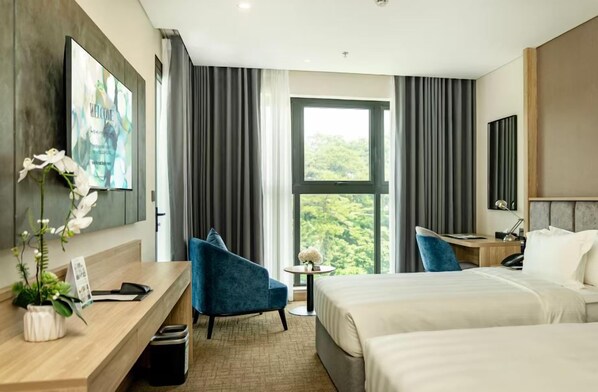 A modern hotel room with a large bed, a desk, a chair, and a view of greenery through the window.