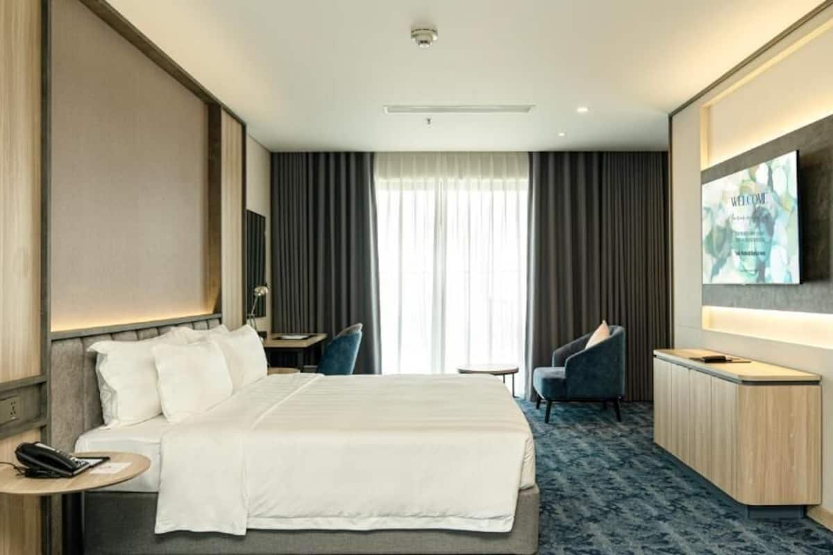 A hotel room with a bed, bedside table, chair, desk, and a large mirror.