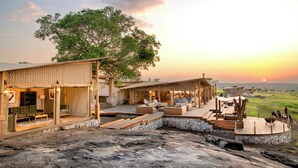 A modern outdoor lounge area with a stone wall, wooden deck, and seating arrangements. - One Nature Mara River (Serengeti)