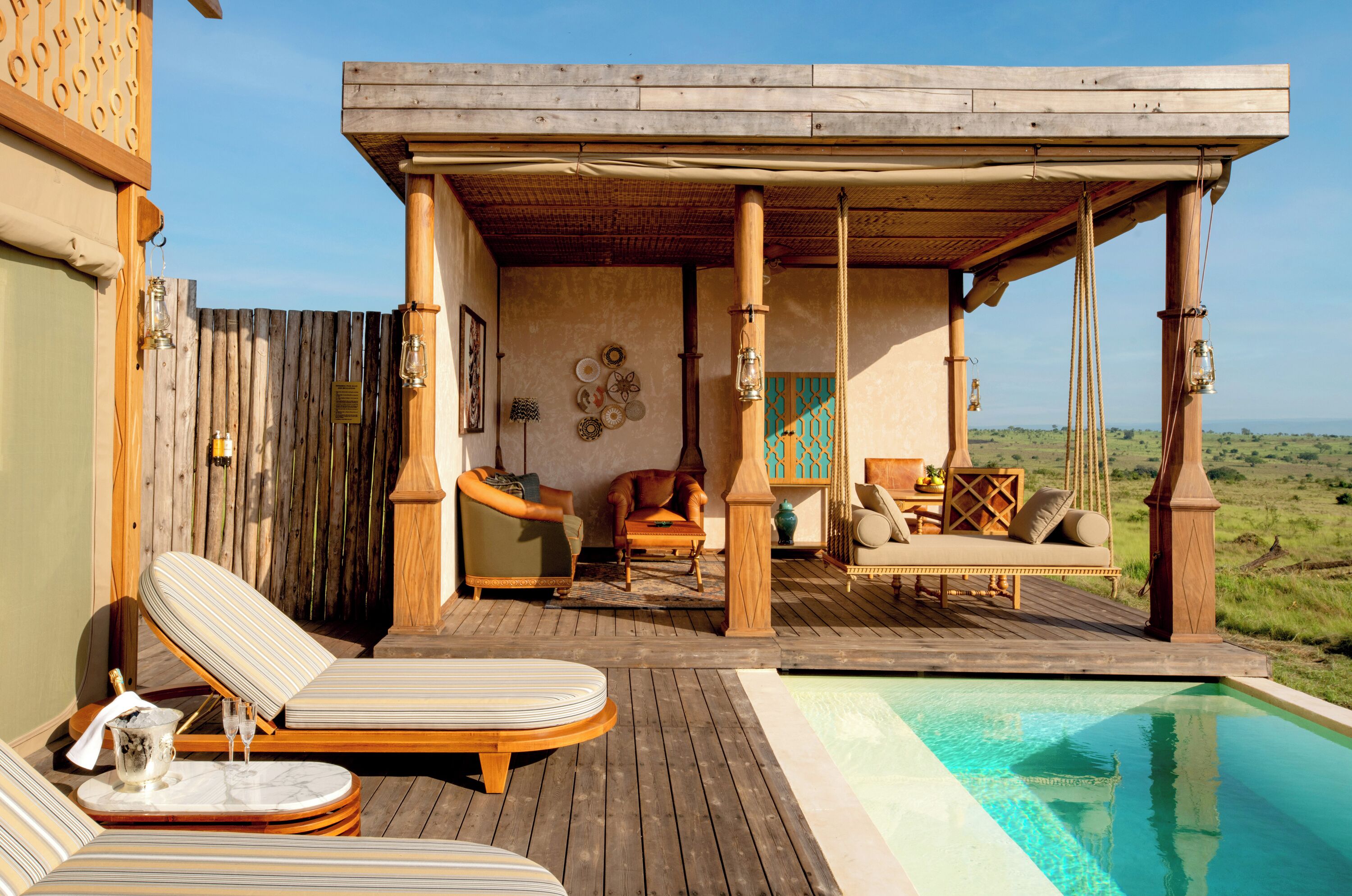 A wooden deck with lounge chairs and a pool, overlooking a grassy landscape.