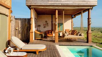A wooden deck with lounge chairs and a pool, overlooking a grassy landscape.