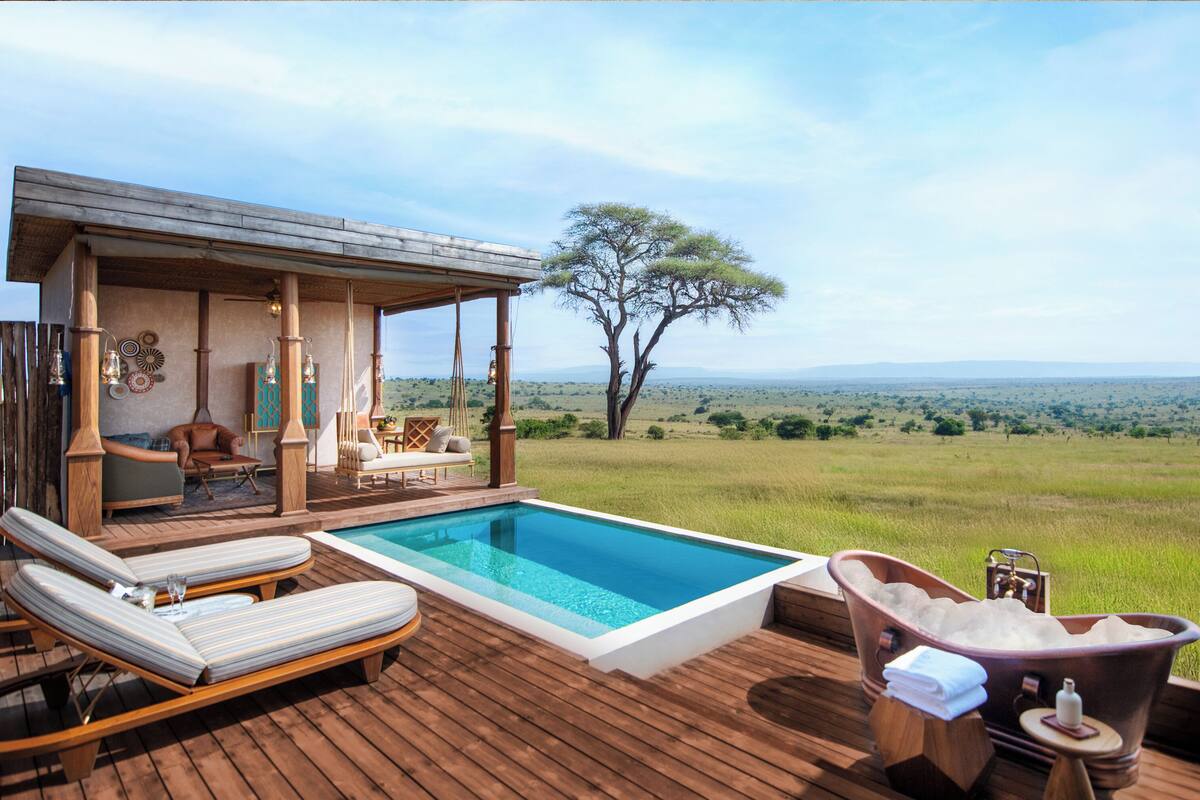A wooden deck with a pool, lounge chairs, a hot tub, and a covered seating area with a view of the savannah.