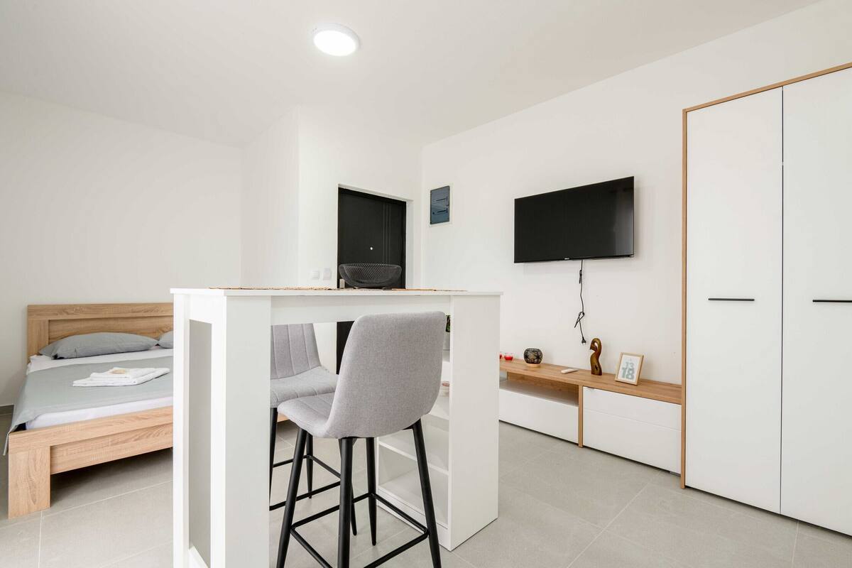 A compact bedroom with a bed, a small desk, a chair, a TV, and a wardrobe.