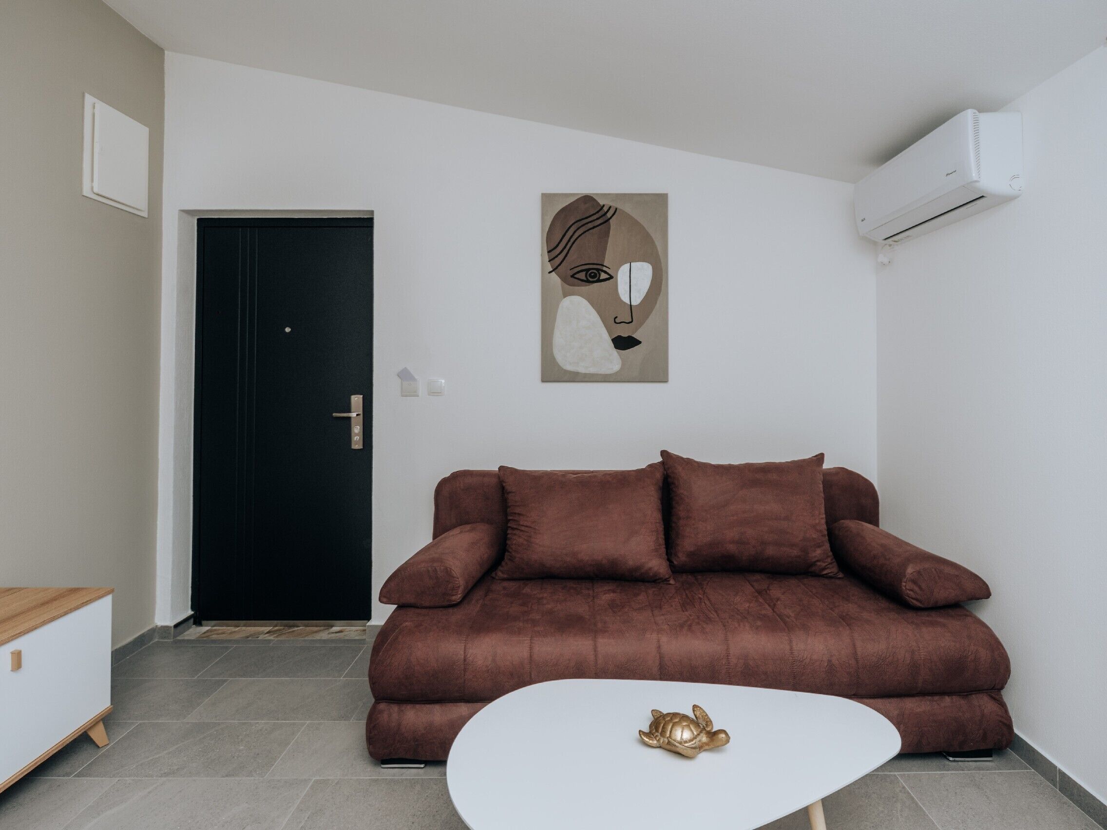 Una sala de estar moderna con un sofá marrón, una mesa de centro blanca y un aire acondicionado instalado en la pared.