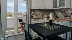 Une cuisine moderne avec des meubles blancs, un pare-feu en marbre et un coin repas comprenant une table et des chaises noires.