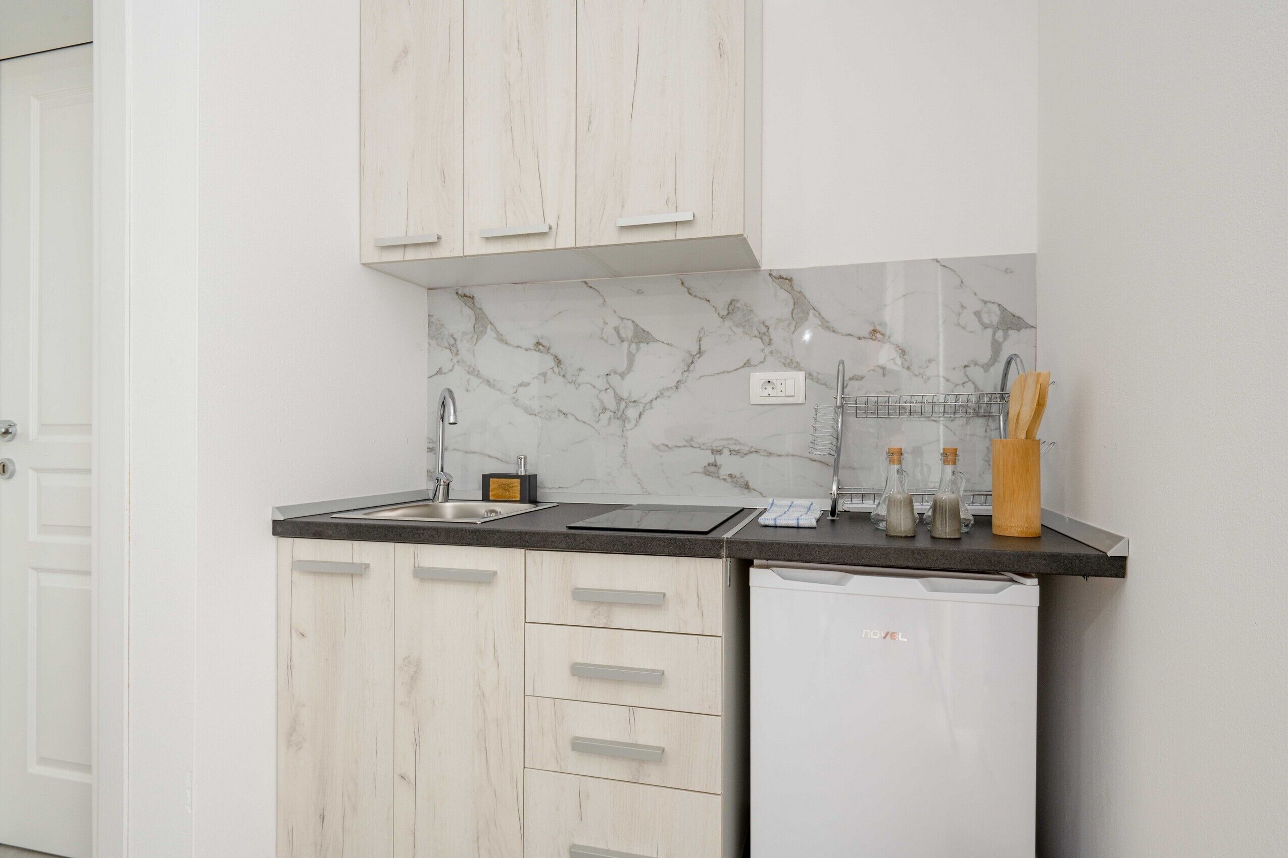 A kitchen with white cabinetry, a marble backsplash, a sink, a dishwasher, and a countertop with utensils.