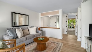 A modern living room with a grey sofa, a round wooden coffee table, and a large mirror on the wall. - Kauai The Cliffs At Princeville 4209 1 Bedroom Condo (Princeville)
