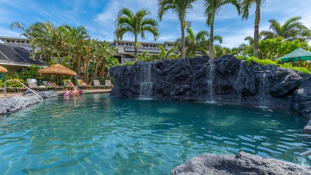 A pool with a waterfall feature, surrounded by palm trees and lounge chairs. - Kauai The Cliffs At Princeville 4209 1 Bedroom Condo (Princeville)