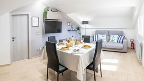 Una moderna zona pranzo con tavolo apparecchiato per quattro persone, un divano grigio e una TV a parete.