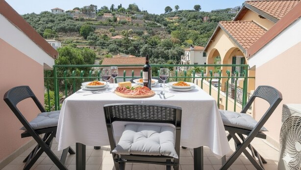 Un tavolo da balcone apparecchiato con piatti di cibo, bicchieri di vino e una bottiglia.