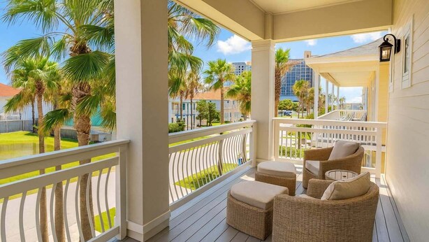 A covered outdoor balcony with wicker furniture and a view of palm trees and buildings. - Padre Beach House 5 Bedroom Home by RedAwning (South Padre Island)