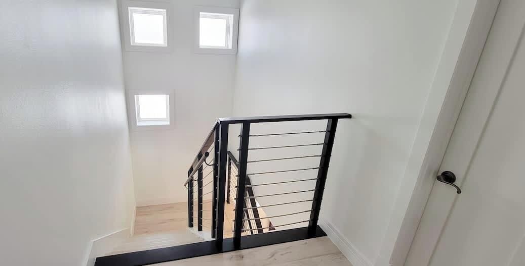 A staircase with a black metal railing, white walls, and a door on the right.