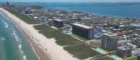 An aerial view of a coastal city with a long beach, buildings, and a bridge in the distance.