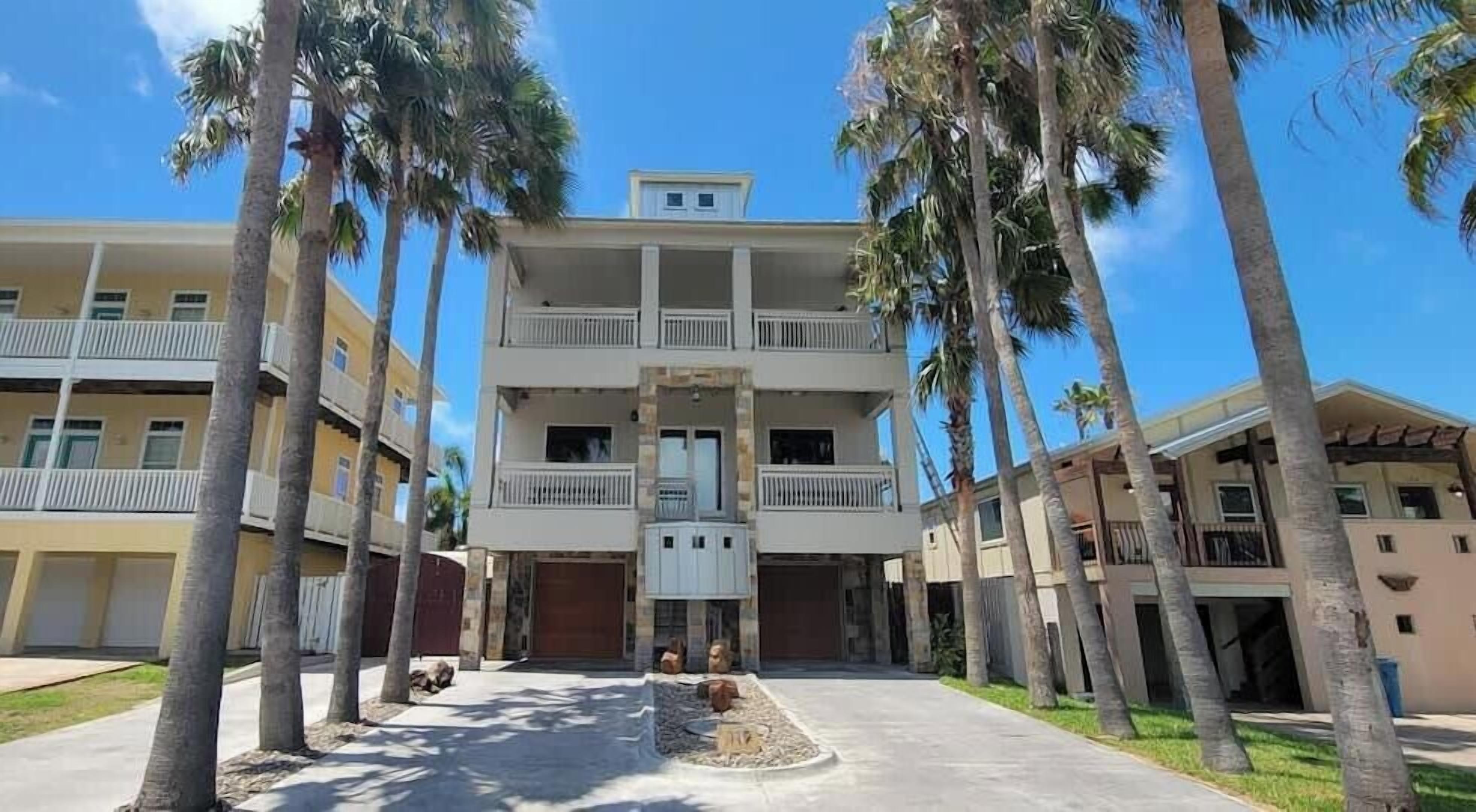 A multi-story hotel with balconies, palm trees, and a clear sky.