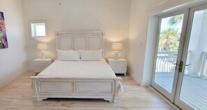 A bedroom with a large bed, two bedside tables with lamps, a window, and a sliding glass door leading to an outdoor area. - Padre Beach House 5 Bedroom Home by RedAwning (South Padre Island)