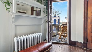 A room with a wooden bench, a radiator, and a view of a balcony with a chair.