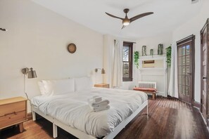 Een slaapkamer met een bed, nachtkastjes, een plafondventilator, een radiator en een raam met gordijnen.