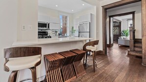 A modern kitchen with a central island, wooden bar stools, and a view into the dining area.