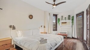 A bedroom with a bed, bedside tables, a ceiling fan, a radiator, and a window with curtains.