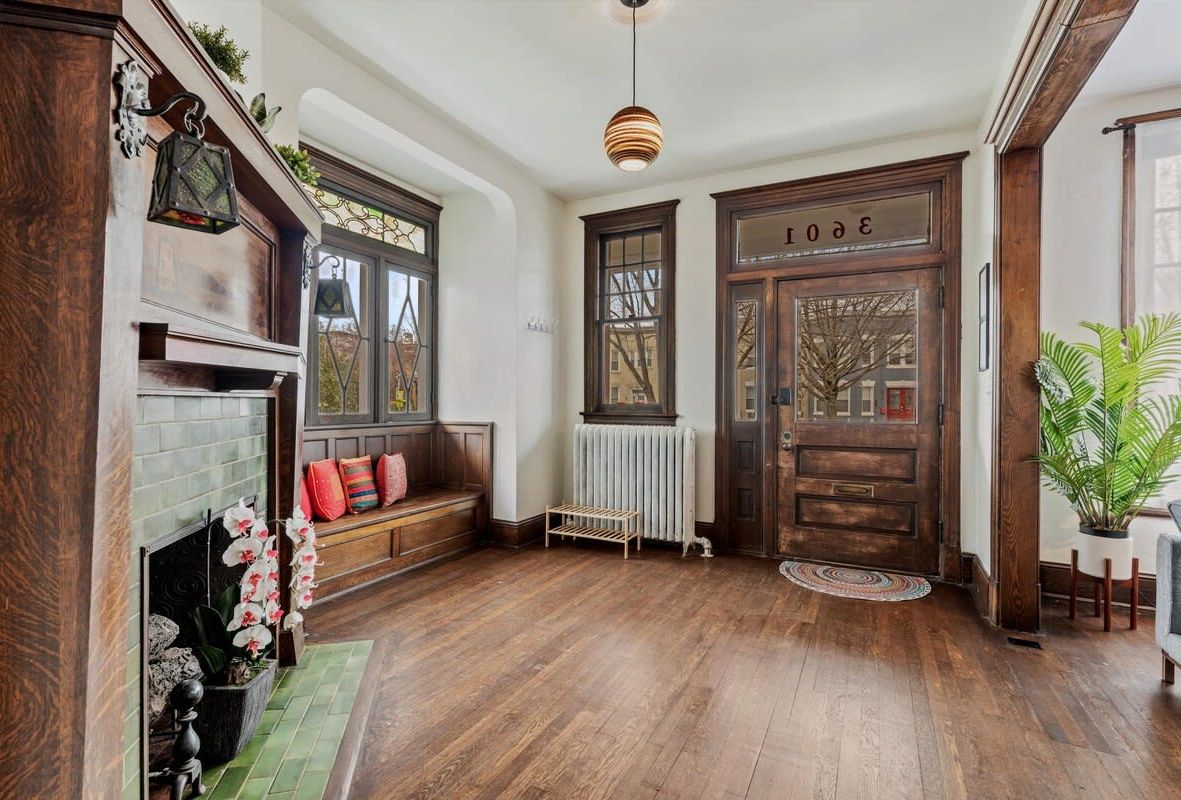 A spacious entryway with a wooden floor, a bench with colorful cushions, a fireplace, and a large wooden door with the number 30.