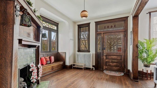 A spacious entryway with a wooden floor, a bench with colorful cushions, a fireplace, and a large wooden door with the number 30.